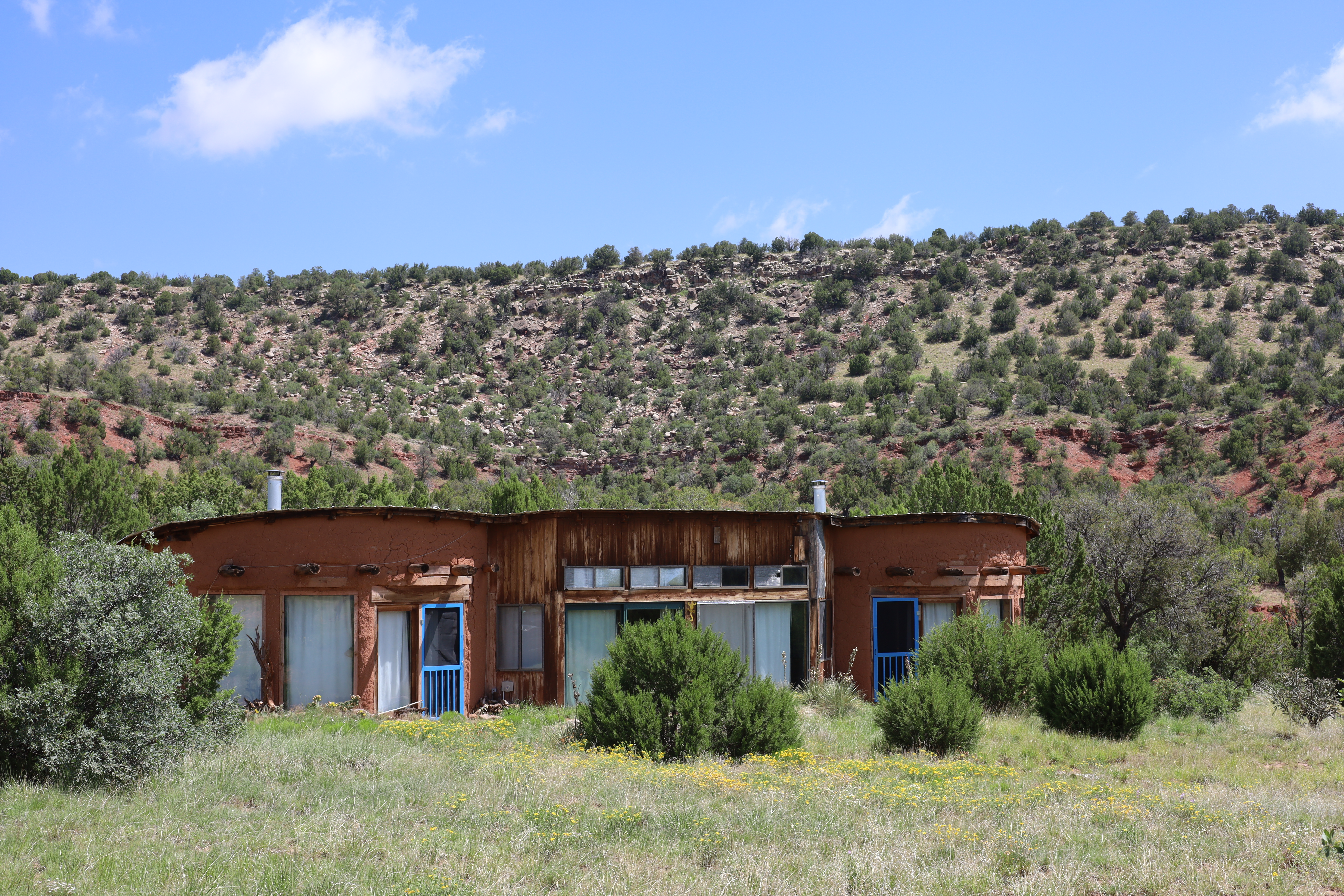A welcoming adobe casita with turquoise doors nestled into a desert shrub hill